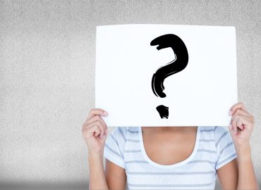 Signo de interrogación pintado en un cartel que sostiene una mujer a la altura de su cara