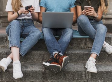 tres jóvenes mirando un ordenador portátil y unos móviles
