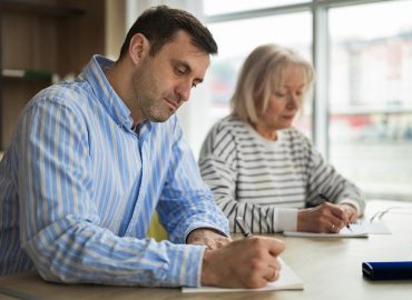 Dos adultos asistiendo a clase toman notas, tras el aumento de matriculaciones