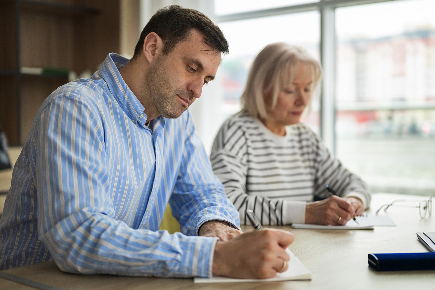 Dos adultos asistiendo a clase toman notas, tras el aumento de matriculaciones
